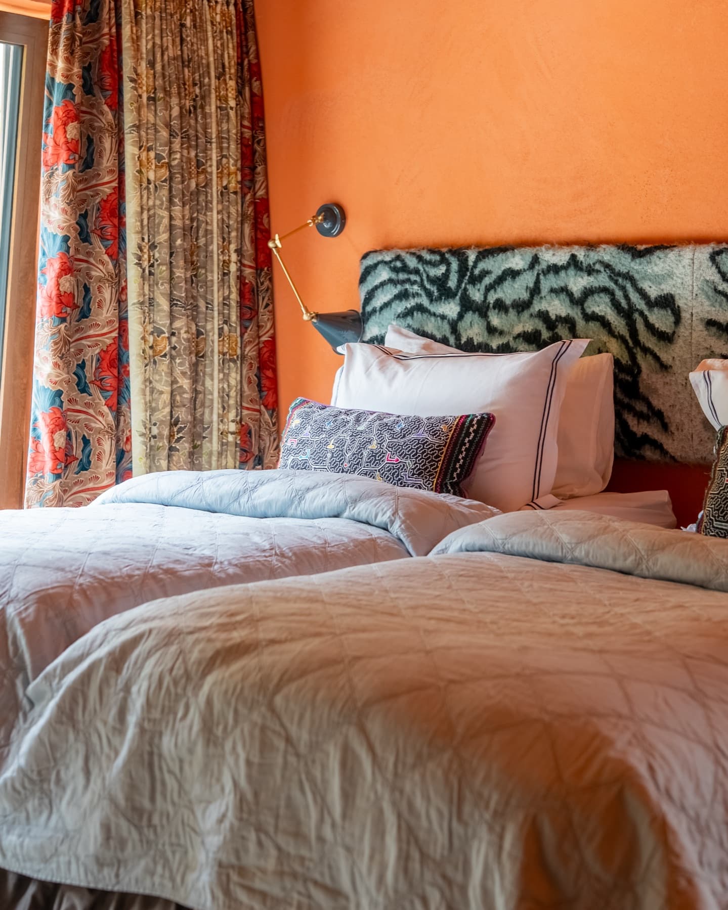Beds made up in white linen against a printed headboard, terracotta walls
