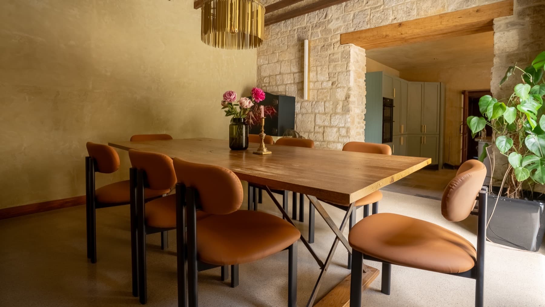 Dining table set for eight beneath a brass pendant, stone wall behind