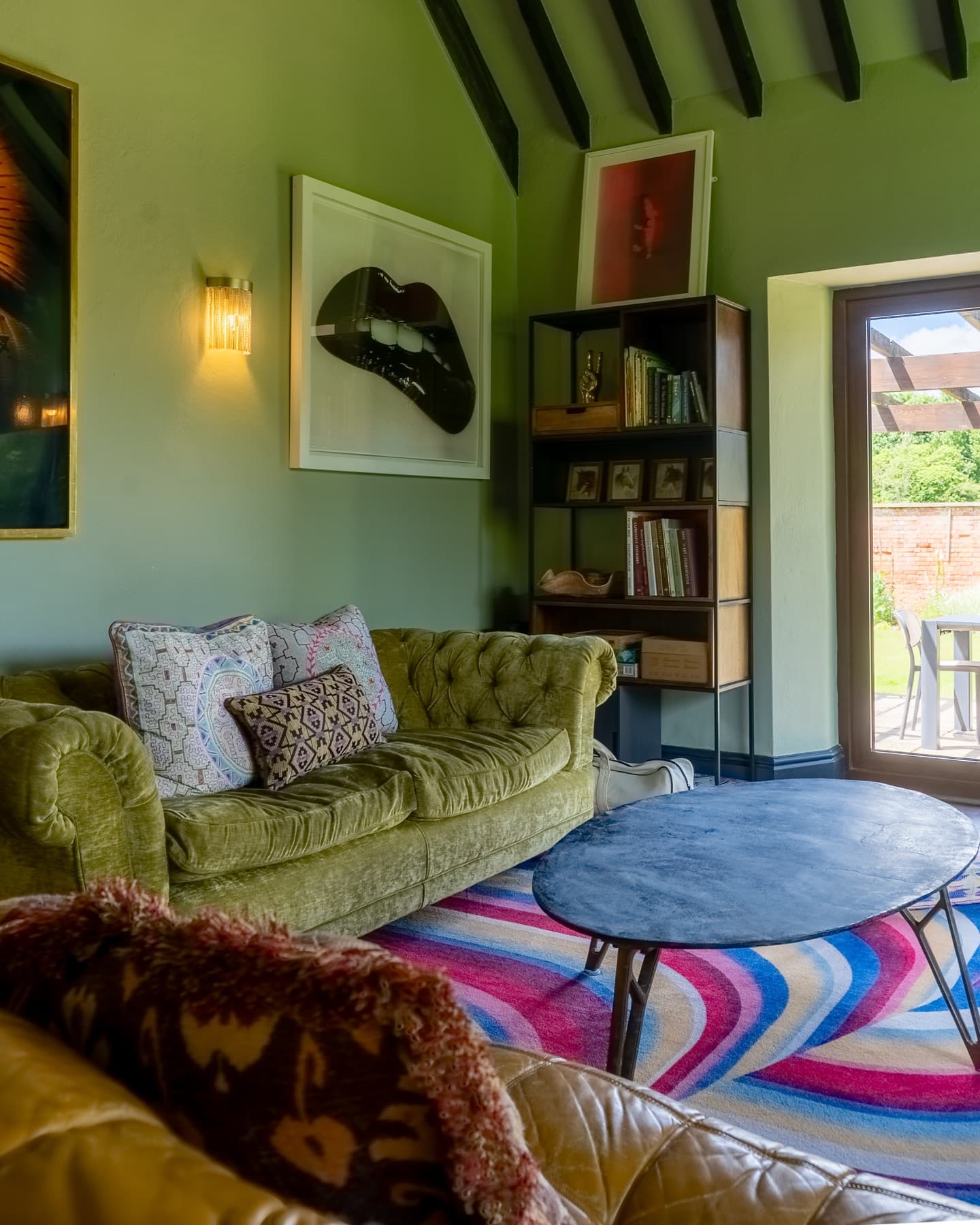 Green velvet sofa below framed prints, terrace doors beyond